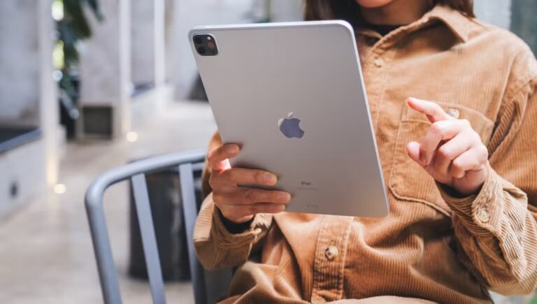 a woman holding an ipad pro with one hand while sitting on a chair